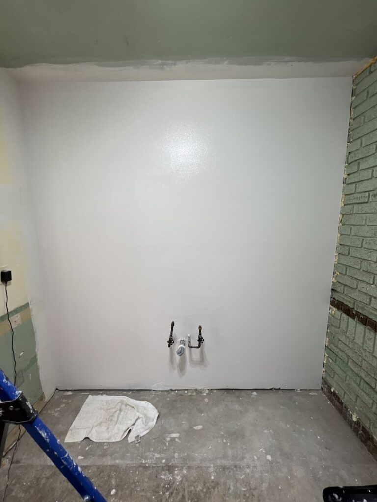 An interior room showing a wall partially painted white over green, with exposed pipes and a ladder, indicating work in progress by OG Renovations in Huntington, WV.
