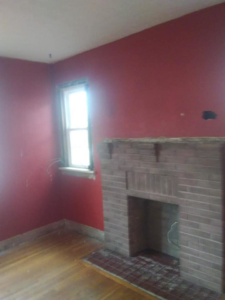 An interior room with red painted walls, a window, and a brick fireplace, indicating a renovation project by Any Length Improvements in Bowling Green, KY.