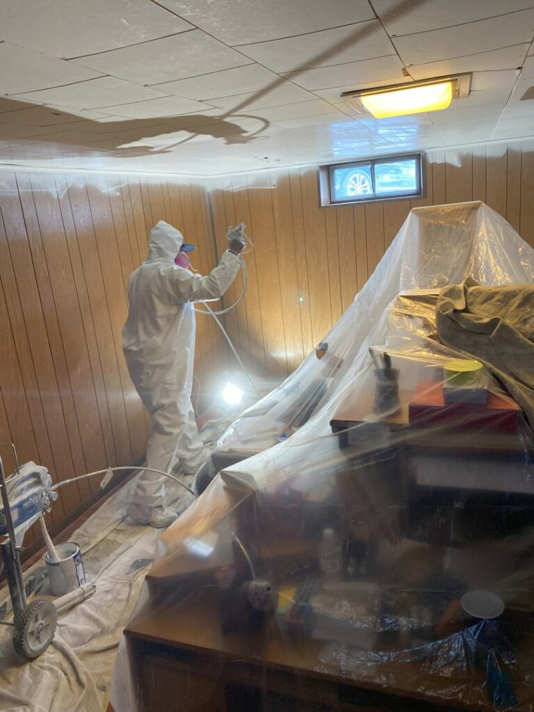 A professional from TD Estimating Group LLC in Springfield, MA, spray painting an interior room with protective gear.