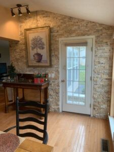 An interior wall featuring decorative stone veneer installation and a glass door, completed by Pink Rose Home Service in Rochester, NY.
