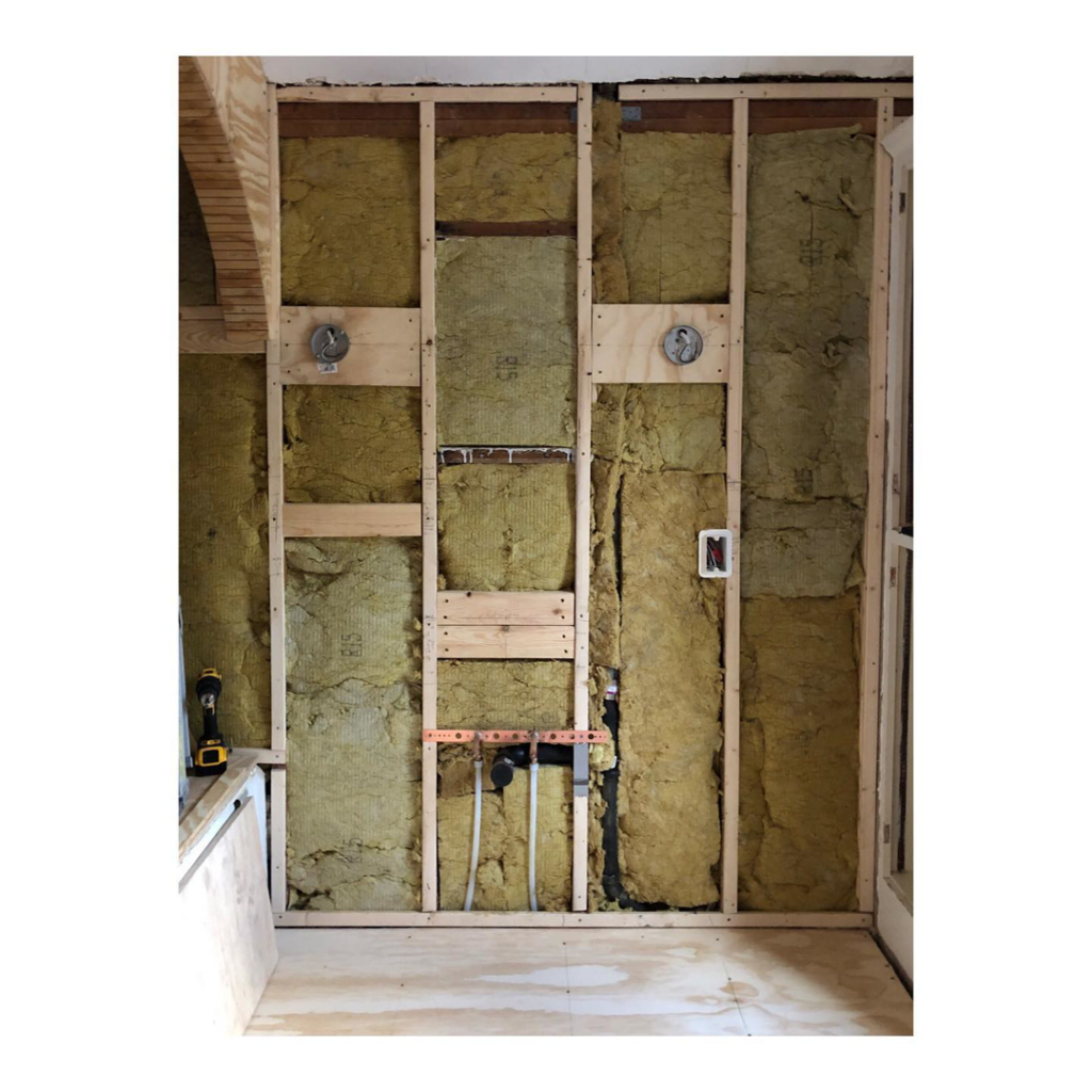 An interior wall under construction with framing, insulation, and plumbing installed by StadlerCraft in Bloomington, MN.