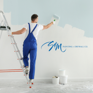 A professional painting an interior wall with a roller on a ladder for S&M Painting and Drywall in Carmel, IN.