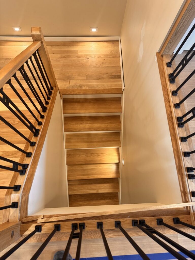A newly installed interior wooden staircase with modern black metal railings, completed by Orion Construction Services in Duluth, MN.