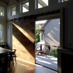 A modern interior featuring a large wooden barn door and hardwood floors, leading to an outdoor deck, by Kaleidoscope Design Build in Houston, TX.