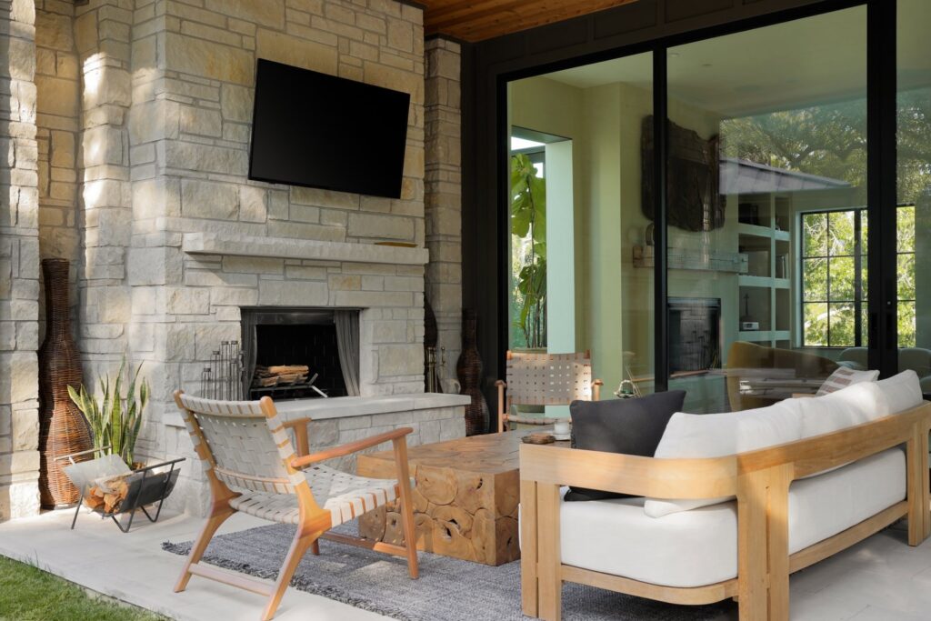 An inviting outdoor patio featuring a stone fireplace, comfortable seating, and a mounted TV by Stone Acorn Builders in Bellaire, TX.
