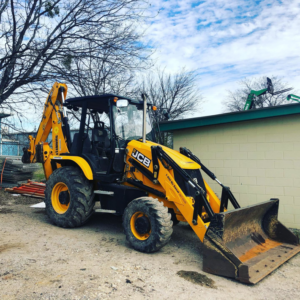 A yellow JCB backhoe loader, heavy construction equipment, parked at a job site by SADE Contractors in San Antonio, TX