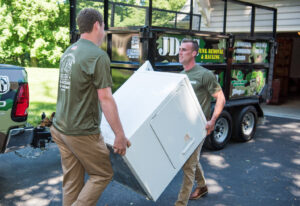 Two JDog Junk Removal & Hauling Capital Region NY crew members hauling a large white appliance to a trailer in Schenectady, NY.