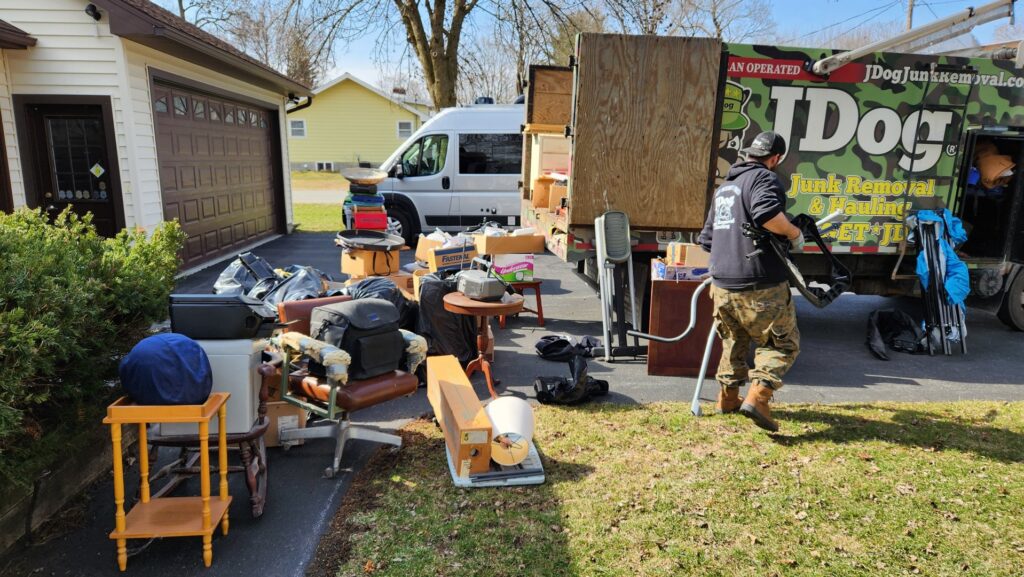 A JDog Junk Removal & Hauling Capital Region NY crew member removing a large pile of various junk items from a lawn in Schenectady, NY.