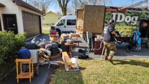 A JDog Junk Removal & Hauling Capital Region NY crew member removing a large pile of various junk items from a lawn in Schenectady, NY.