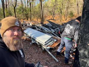 A JDog Junk Removal & Hauling Concord, NC crew member clearing a large pile of debris from a wooded area.