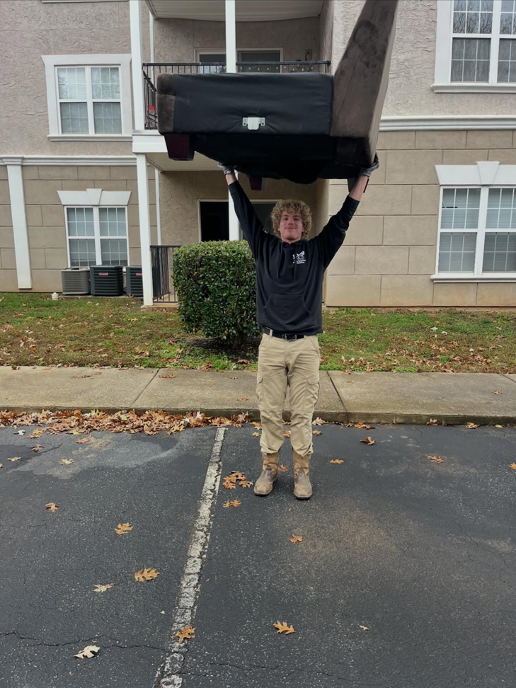 A JDog Junk Removal & Hauling Concord, NC team member expertly removing a large, old sofa from an apartment complex.