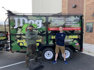 Two team members from JDog Junk Removal & Hauling Concord, NC, standing proudly in front of their branded junk removal trailer.