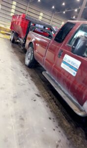 A Jedi Junk Removal Garbage Services Pocatello, ID, truck towing a red roll-off dumpster on a trailer.