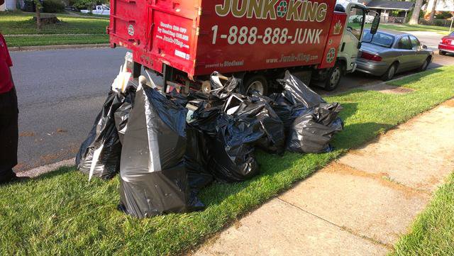 Black trash bags piled on the grass next to a Junk King truck for removal in Greensboro, NC.