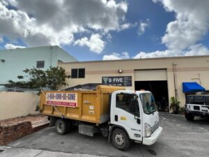 A Junk Be Gone branded junk removal truck parked outside a commercial building in Miami, FL.