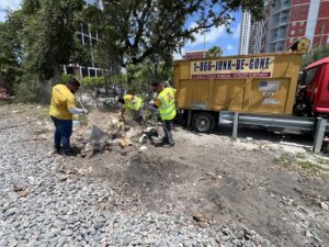 Junk Be Gone crew members in yellow vests raking and cleaning debris next to their junk removal truck in Miami, FL.