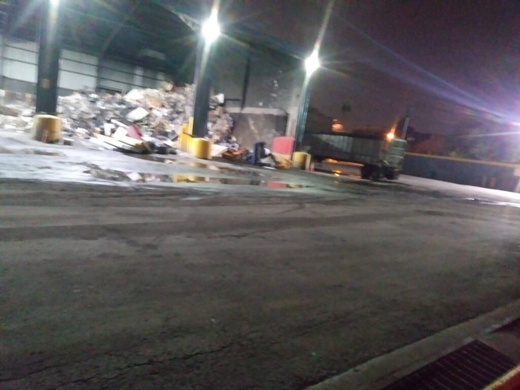 A junk processing facility with a scissor lift, truck, and piles of waste, demonstrating Lemcor's operations in Newark, NJ.