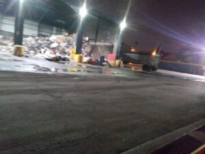 A junk processing facility with a scissor lift, truck, and piles of waste, demonstrating Lemcor's operations in Newark, NJ.