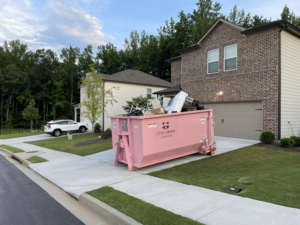 A pink dumpster from Little Junkers filled with various junk items in a residential driveway in Peachtree City, GA.
