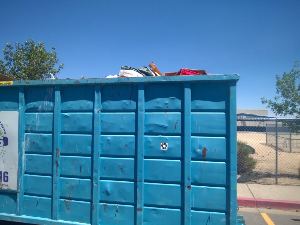 A large blue roll-off container from Empire Waste Systems in Carson City, NV, filled with various junk items