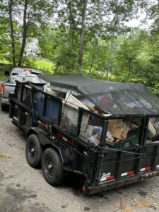 A Rubbish Doctor trailer filled with various junk and covered with a tarp, being towed on a residential street in Portland, ME.