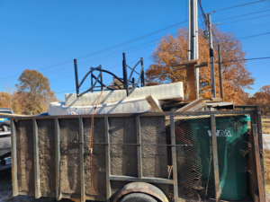A junk-filled trailer containing a mattress, metal frames, and other debris, hauled by Urban Junk Removal, LLC in Springdale, AR.
