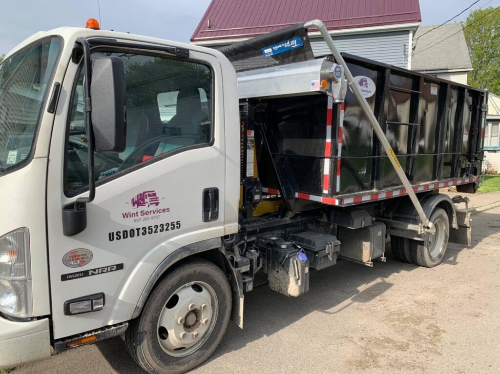 A white junk hauling truck with a black dumpster from Wint Services, LLC, parked on a residential street in Colorado Springs, CO.