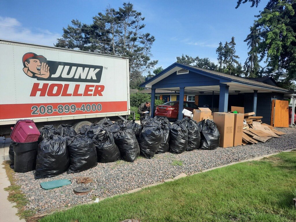 A Junk Holler truck parked next to a large pile of trash bags and cardboard boxes for removal in Boise, ID.