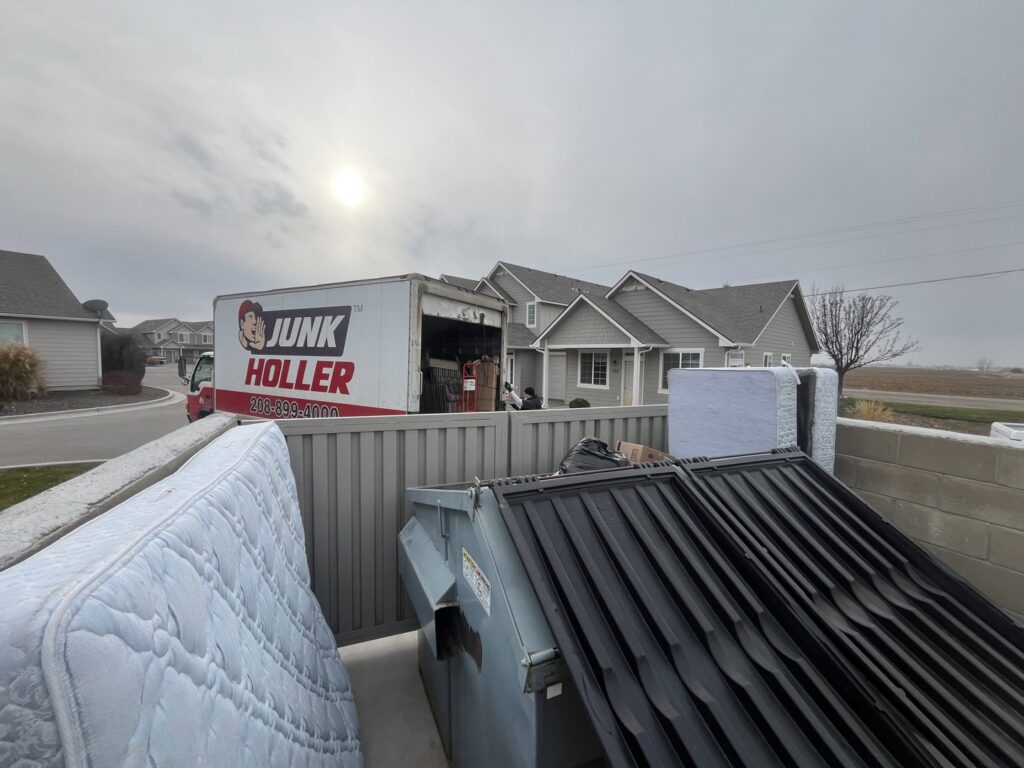 A Junk Holler truck parked near a large dumpster and old mattresses at a junk removal site in Boise, ID.