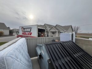 A Junk Holler truck parked near a large dumpster and old mattresses at a junk removal site in Boise, ID.