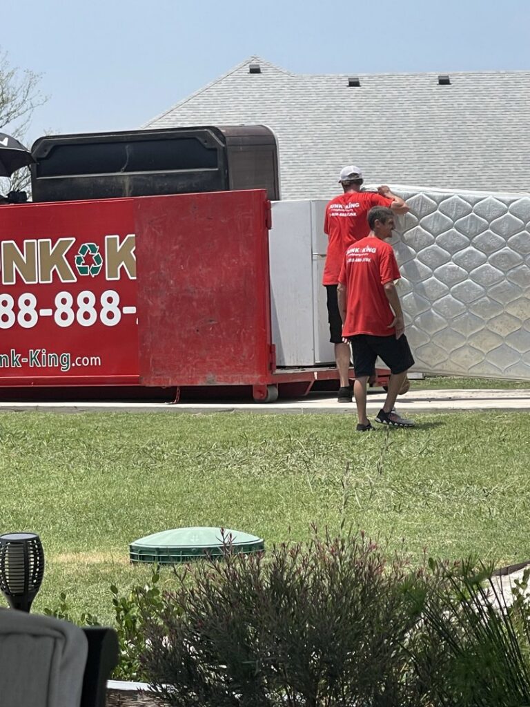 A Junk King Plano, TX crew member loading a large mattress into the back of a junk removal truck.