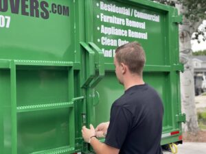A Junk Movers employee closing the back door of a green junk removal truck in Salt Lake City, UT, after loading items.
