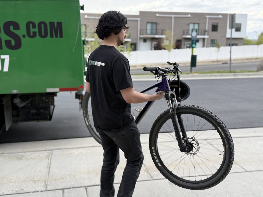 A Junk Movers employee carrying a bicycle towards a junk removal truck in Salt Lake City, UT, during a service job.