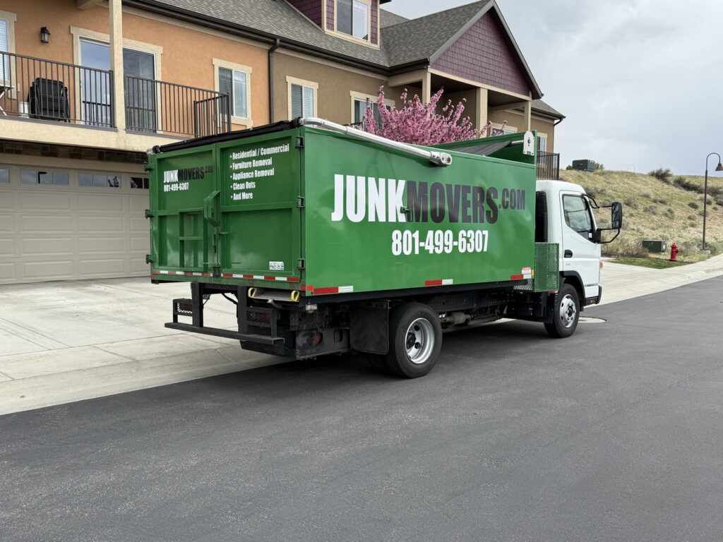 A green Junk Movers truck with branding and services listed, parked on a residential street in Salt Lake City, UT.