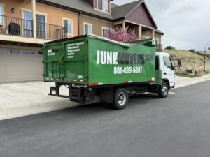 A green Junk Movers truck with branding and services listed, parked on a residential street in Salt Lake City, UT.