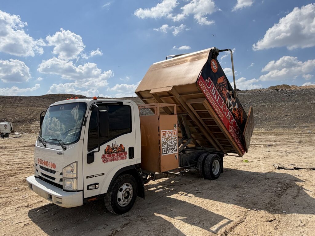 A Junk Out Boyz LLC truck with its dump bed raised, disposing of collected junk at a facility in Georgetown, TX.