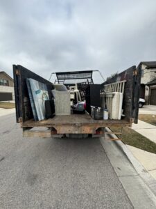 The back of a Junk Out Boyz LLC truck loaded with household junk, including furniture and boxes, in Georgetown, TX.