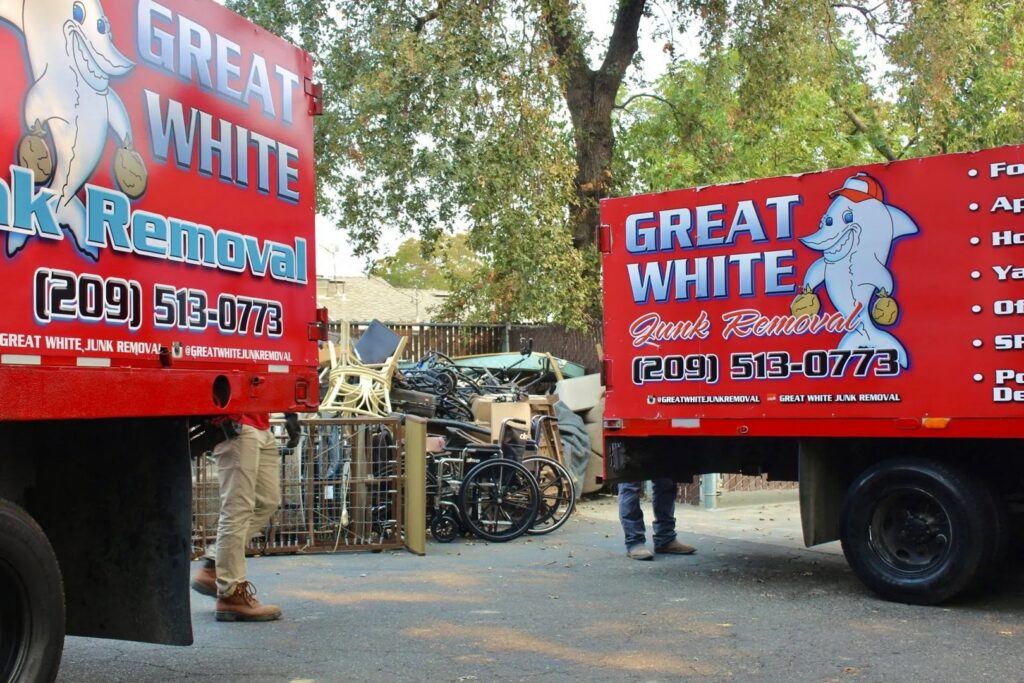 A pile of junk, including wheelchairs and chairs, located between two Great White Junk Removal trucks in San Francisco, CA.