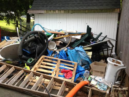 A pile of junk including a ladder, wooden pallets, and hoses next to a white shed, removed by Avery's Junk Removal & Hauling in Trenton, MI.