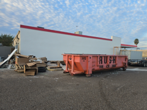 A large pile of cardboard boxes and debris next to a Rush Disposal LLC dumpster for junk removal in Laredo, TX.