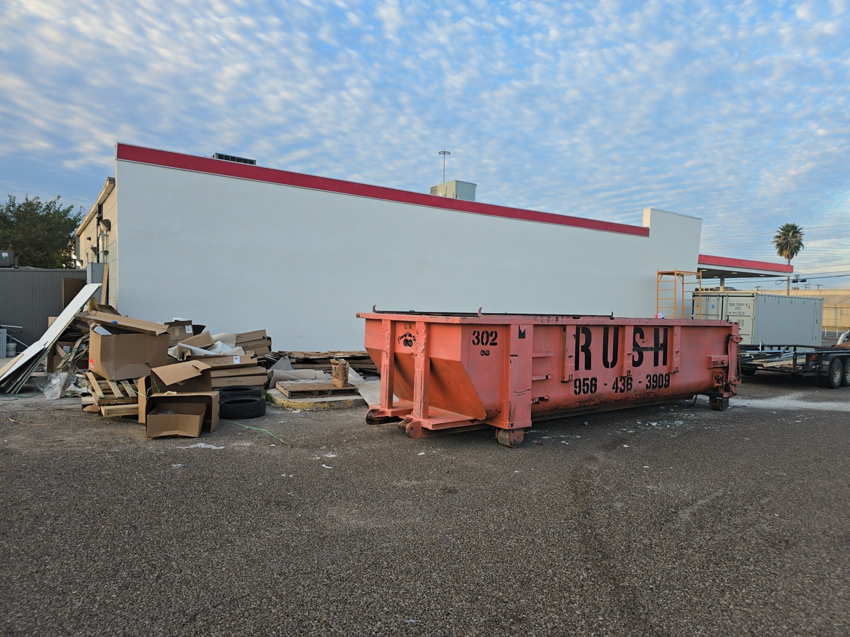 A large pile of cardboard boxes and debris next to a Rush Disposal LLC dumpster for junk removal in Laredo, TX.