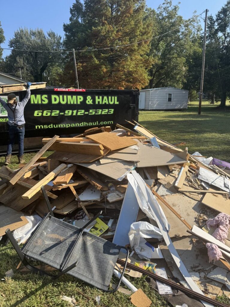 A large pile of construction debris and junk on the ground with an MS Dump & Haul dumpster in the background in Hernando, MS.