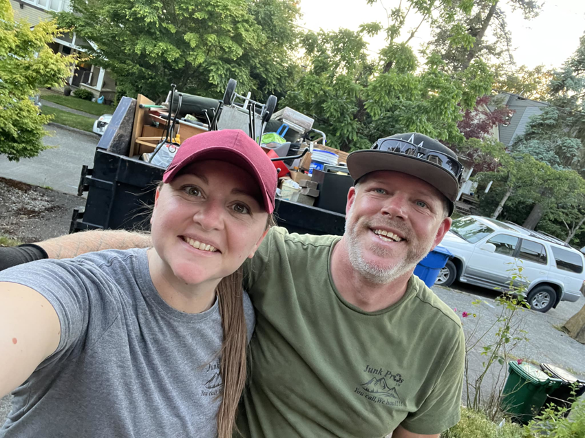 Two smiling Junk Pros NW team members standing in front of a truck loaded with junk in Bellevue, WA.