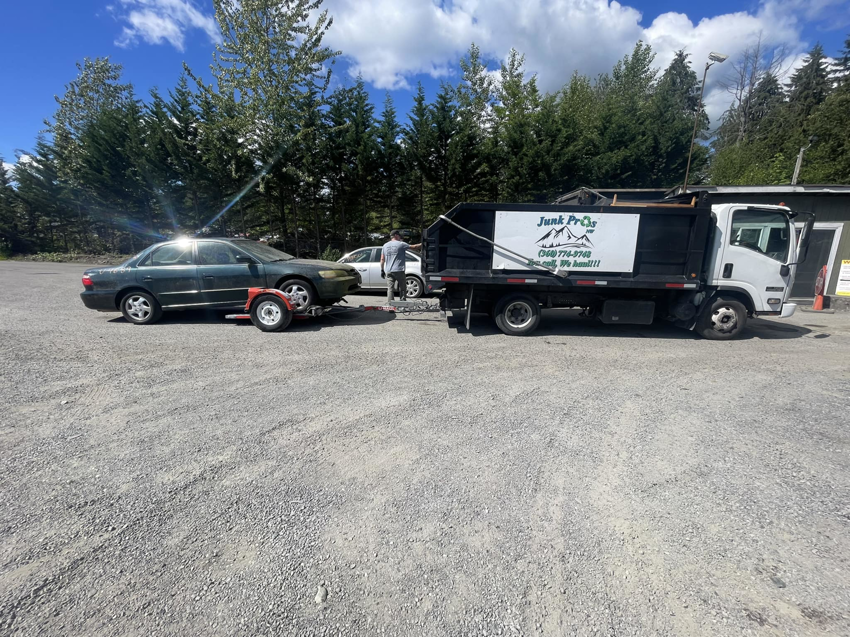 A Junk Pros NW truck towing a car on a trailer, providing vehicle removal services in Bellevue, WA.