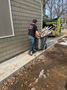A Junk It OR Dump It crew member in Independence, MO, pushing a bin full of debris towards a junk removal truck.