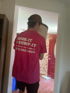 A Junk It OR Dump It crew member in Independence, MO, carrying a rolled-up rug out of a house for disposal.