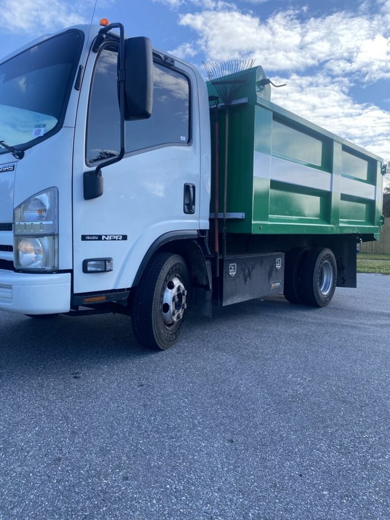 A green and white dump truck, equipped with tools, used for junk removal services by The Removal Squad LLC in Orlando, FL.