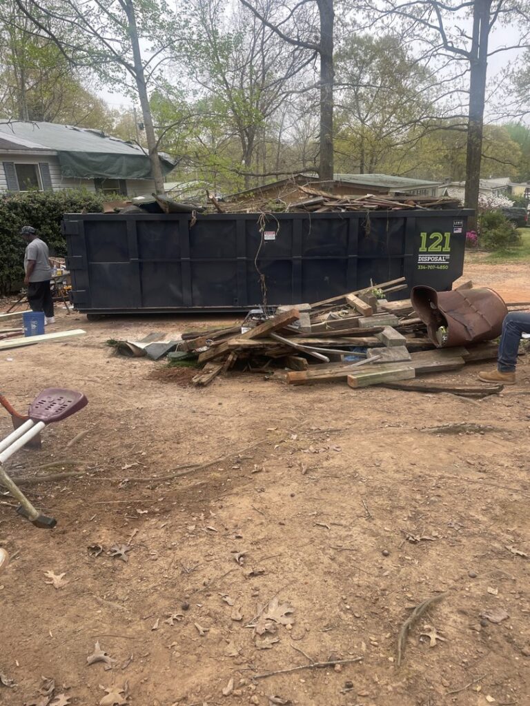 A large roll-off dumpster from 121 Disposal Co. placed next to a pile of wood and general debris for junk removal in Columbus, GA.