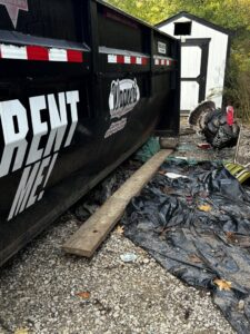 A black roll-off dumpster from Wagners Property Services LLC next to a pile of debris and trash, ready for general junk removal in Canton, OH.