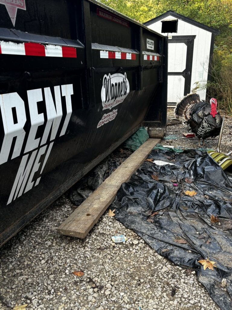 A black roll-off dumpster from Wagners Property Services LLC next to a pile of debris and trash, ready for general junk removal in Canton, OH.